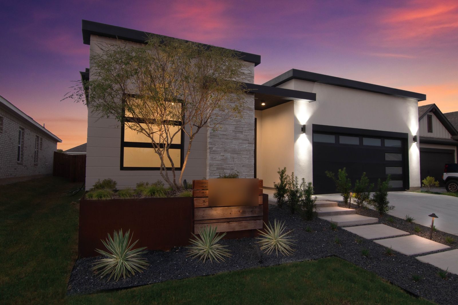 Modern single-story factory-built home at dusk with warm exterior lighting