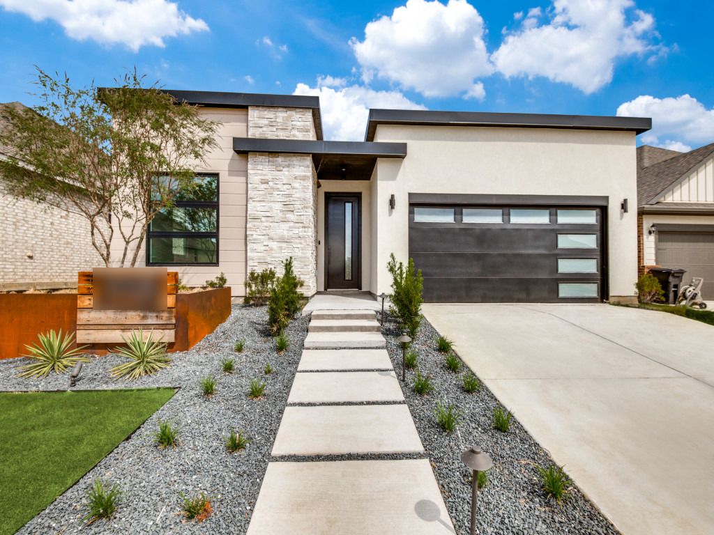 Modern single-story home with white stone, a black garage door, and a landscaped front walk under blue sky